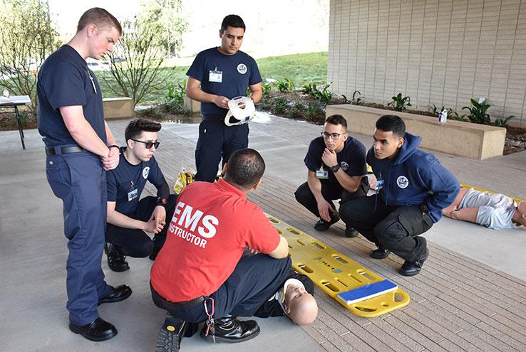 Crafton Hills College EMS students gathered around an instructor demonstrating patient care on a training mannequin strapped to a backboard.