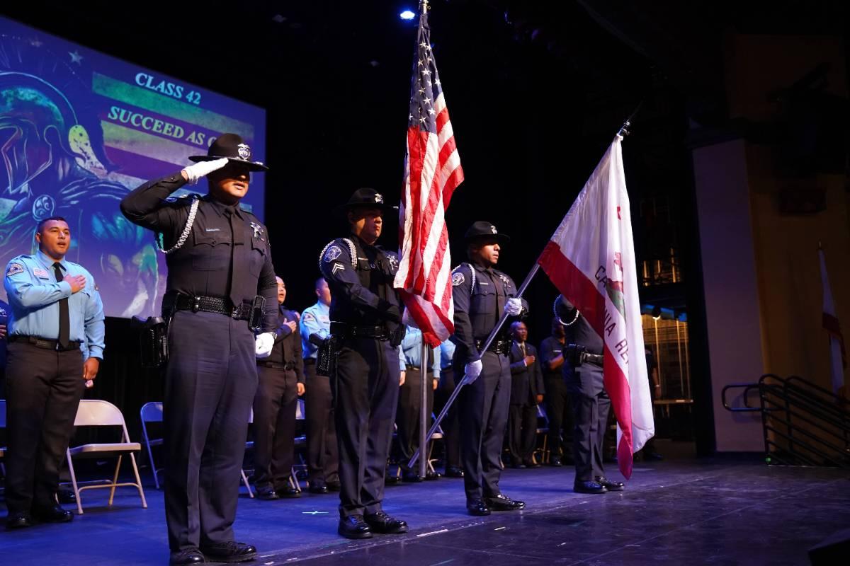San Bernardino Valley College police academy cadets presenting the U.S. and California flags as a cadet salutes during a graduation ceremony.