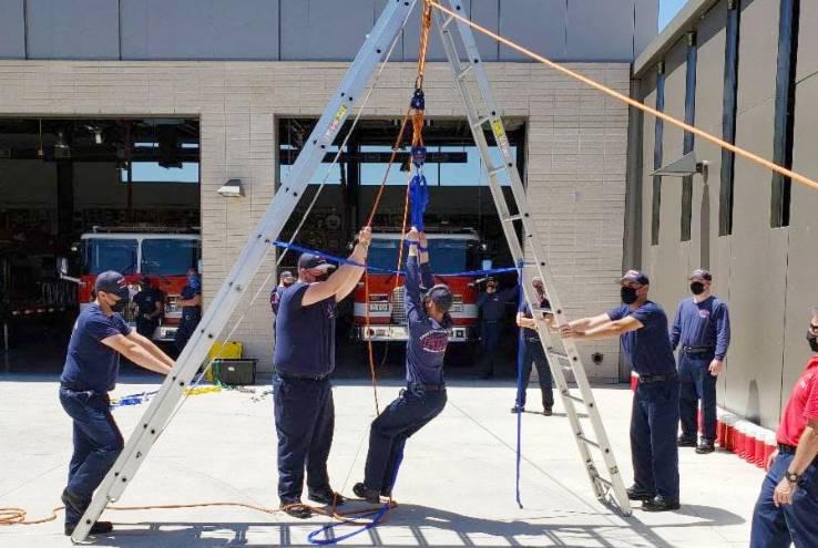 Crafton Hills College fire academy students practicing a rope rescue with a ladder A-frame in front of a fire station.