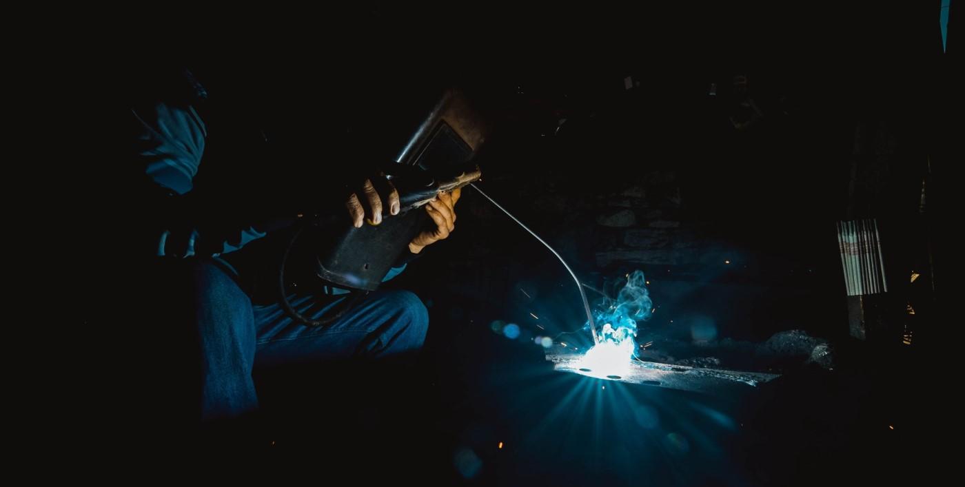 A welding student at work, the bright blue arc and sparks lighting up a dark shop.