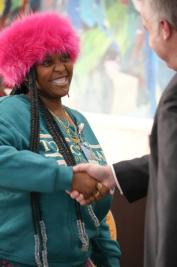 Two people shaking hands, one wearing a pink fuzzy hat and teal sweatshirt.